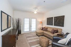 Living room with ceiling fan, neutral walls and carpet, facing two glass doors leading to patio 