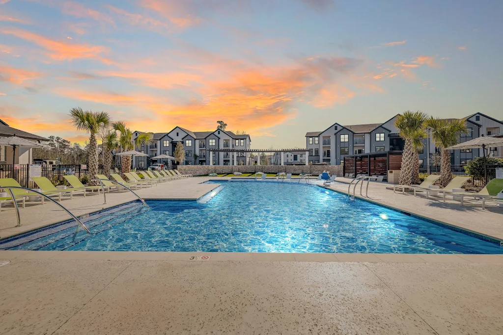 Swimming pool with steps into the pool and lounge chairs nearby with apartment buildings in the background at dusk