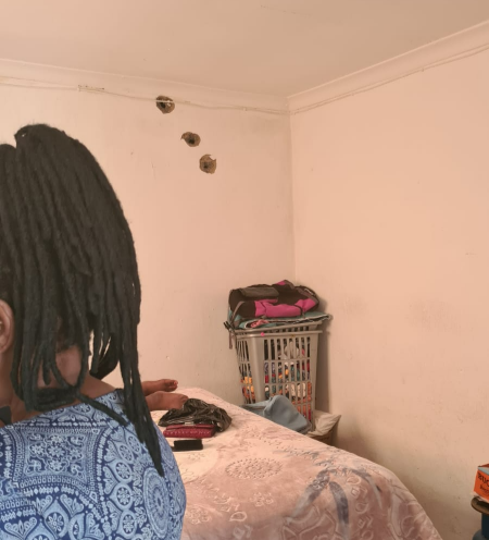 Betty Shezi, 60, who did not want her face identified, in front of bullet holes in her home. Her teenage daughter was in the room when the shootout took place at around 4pm.