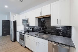 Kitchen with black subway tile backsplash, stainless appliances, white cabinets, and black granite countertops