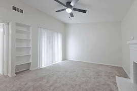 Spacious, bright apartment living room with carpet, ceiling fan, built-in shelves, large window, and a fireplace.