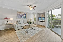 Bright apartment living room with sofa, TV, and balcony access, featuring modern decor and ceiling fan.