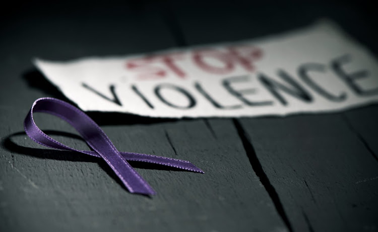 A purple ribbon for the awareness about the unacceptability of the violence against women and the text stop violence on a piece of paper, on a dark gray rustic wooden surface.