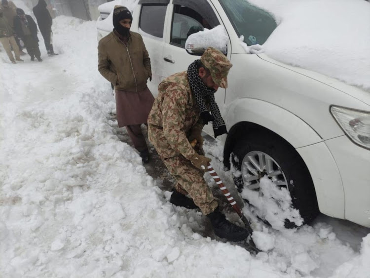 A soldier clears snow under a stranded vehicle after a heavy snowfall in Murree, Pakistan January 8, 2022.