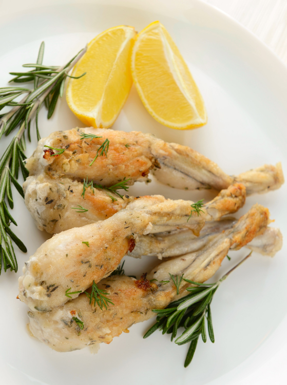 Frogs' legs fried with garlic, lemon and herbs. Stock photo.