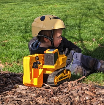 Tree Pros apprentice helper playing with his trucks while dad works in the tree