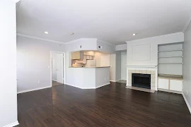 Open concept living room with wood-inspired flooring, built-in shelving, fireplace, and view of the kitchen area