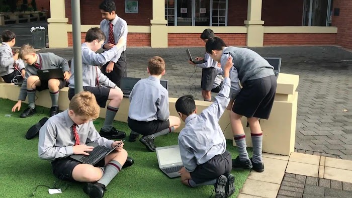 Male students in school uniforms working on laptops in outdoor patio