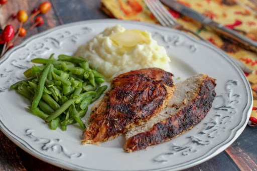 Slices of herb rotisserie turkey breast on a plate with green beans and mashed potatoes.