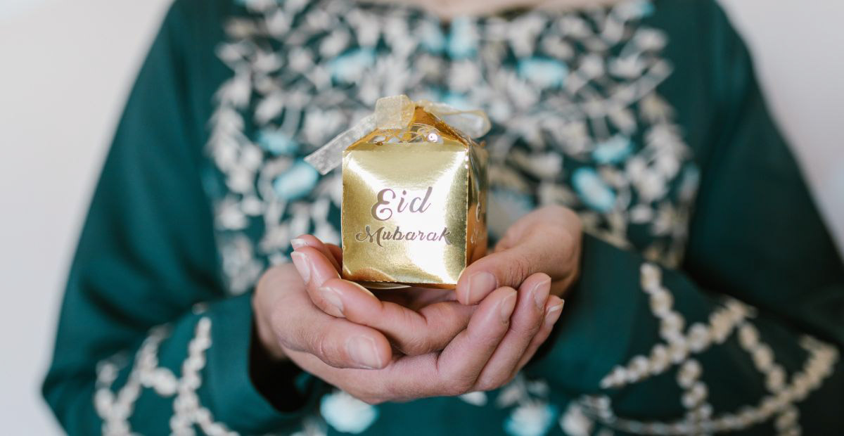 Woman holding small gift box with text "Eid Mubarak" on it