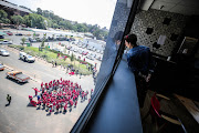 A staff member at Hill on Empire watches on as members of the EFF protest alongside members of the BLF outside the commission of inquiry into state capture in Parktown, Johannesburg, on Monday. 