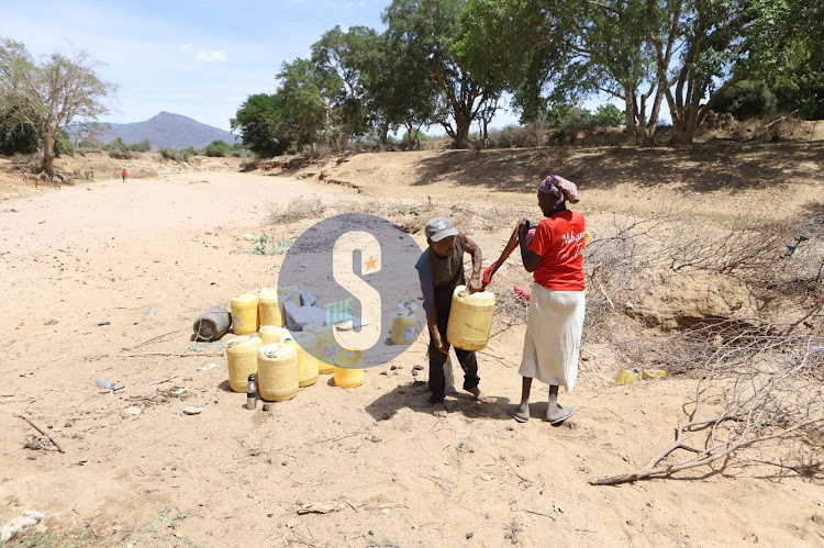 John Kamau helps Rose Kaluma load a water jerican at a well on dried up Voi River, Mwatate, Taita Taveta on November 3, 2022.