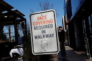 A sign requiring the wearing of a protective face mask is seen as a waiter stands outside a restaurant in Manhasset, New York, US March 29, 2021. 