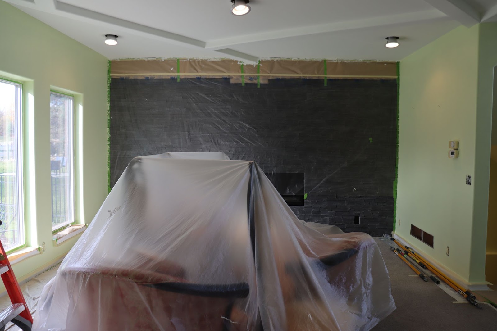 Furniture covered with a plastic tarp inside a house with green walls and a freshly painted white ceiling.