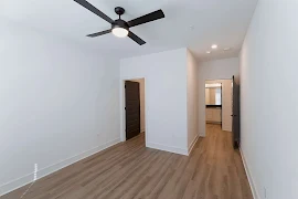 Bedroom with walk-in closet, en suite bathroom, ceiling fan, wood plank floors, black doors, and white walls