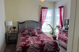 Cozy apartment bedroom with a queen-sized bed, red bedding, matching curtains, a dresser, and a mirrored nightstand.