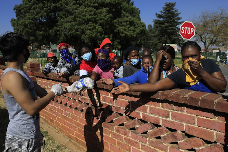 People stand in a line , and wait as volunteers with the grassroots charity ,Hunger has no Religion , hands out food parcels, clothes and toys, in Johannesburg, on June 9, 2020 Hundreds of beneficiaries throughout the neighbourhood of Coronationville reciev food on a daily basis. South Africa is currently at level 3 lockdown to try and curtail the spread of the Covid-19 pandemic.