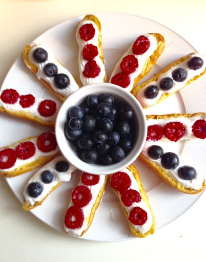 Cream filled eclair halves topped with fresh raspberries and blueberries.