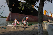 A woman with two children walk past a cargo ship heading to load grains in Reni, Ukraine, on July 27 2022 in Sulina, Romania. Exporters, logisticians, traders, transporters are working to overcome the blockages at the major Black Sea ports with Romania's small Danube ports as outlets for Ukrainian grain and other commodities that have been blocked since the Russian invasion.