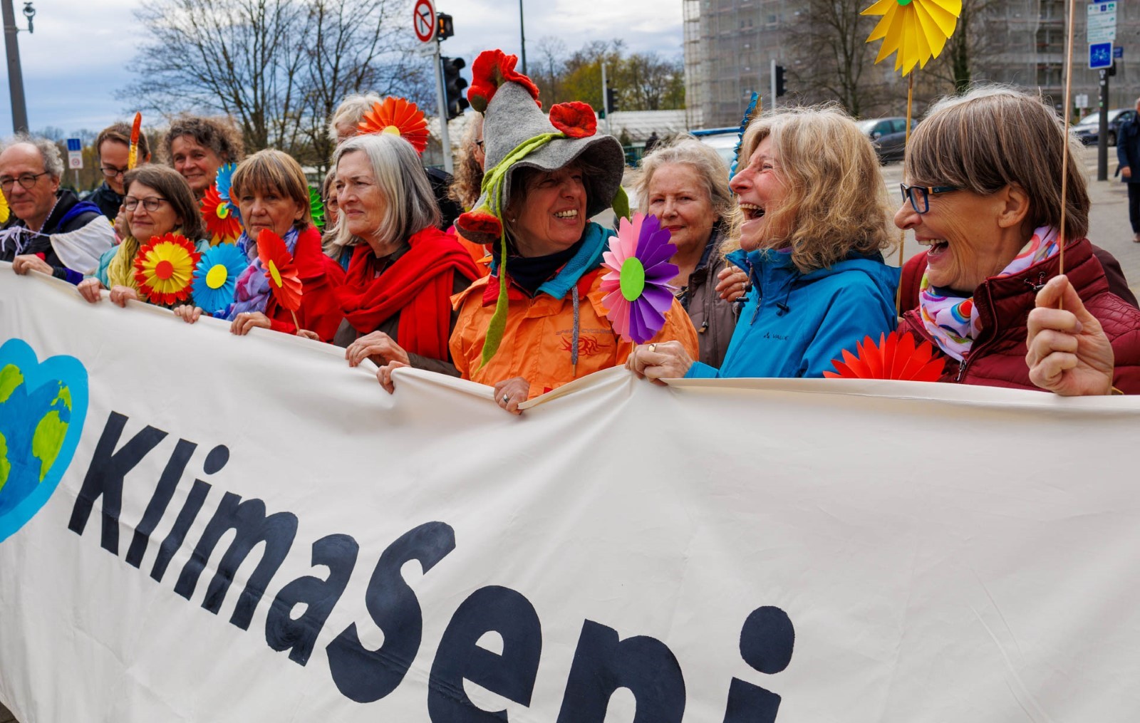 Pensjonister i fargerike klær, med banner og papirblomster i hånden har møtt opp for å støtte saksøkerne fra Klimaseniorinnen utenfor Den europeiske menneskerettighetsdomstolen i Strasbourg (EMD).