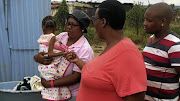 A malnourished girl is carried by Limakatso Selisa, with Vivian Mothijoa in tow. The child cannot access the grant because her mother has no ID.