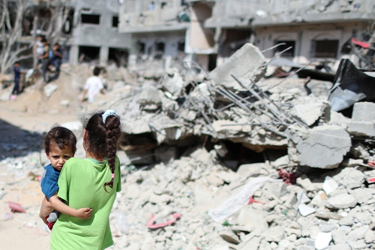 A Palestinian girl carries a boy amid the rubble of their houses which were destroyed by Israeli air strikes during the Israel-Hamas fighting in Gaza on May 23 2021.