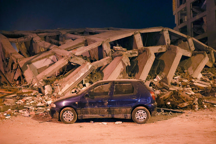 A car parks next to a collapsed building in the city of Adıyaman in Türkiye