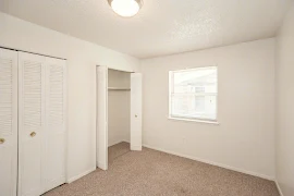 Carpeted bedroom with overhead lighting, a window and two double-door closets 