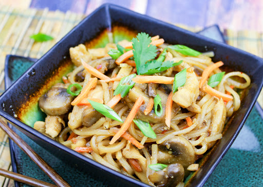 Dragon noodles with chicken in a bowl with scallions sprinkled on top.