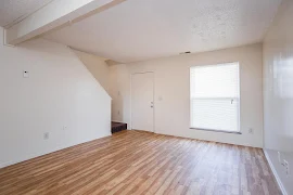 Living room including front door, wood-inspired floors, window with blind, stairwell, white walls and trim