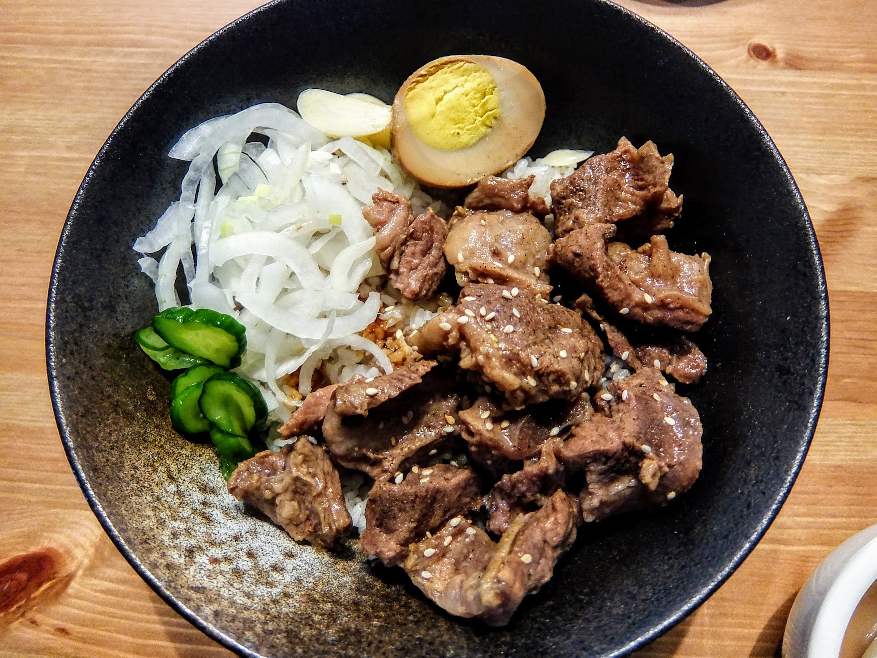 半筋半肉蓋飯,上方有許多洋蔥/半顆滷蛋/黃瓜和牛肉