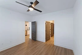 Bedroom with en suite bathroom, wood plank flooring, black doors, white trim and walls, and ceiling fan