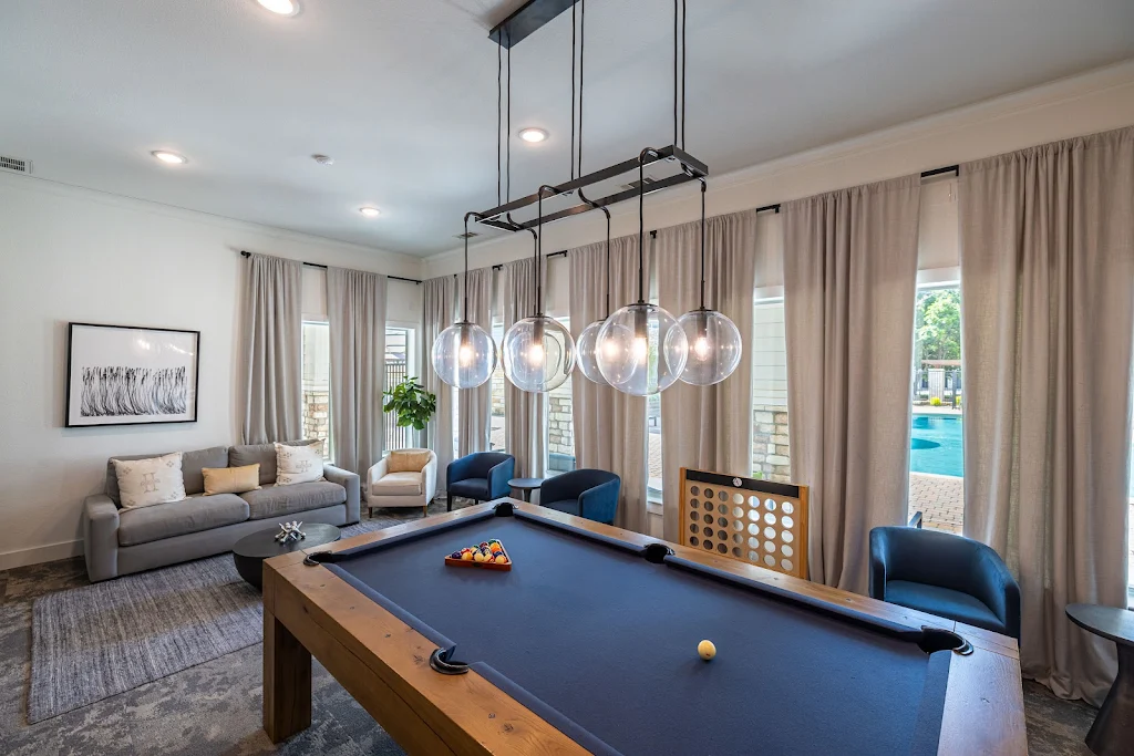 Stylish pool table with modern light fixture in clubhouse, with scattered seating and a large connect 4 game.