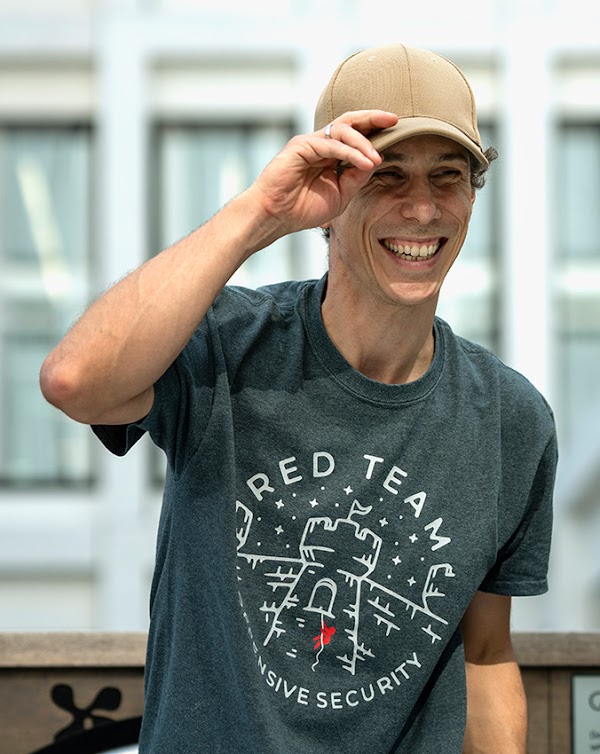 Daniel Fabian, de la Red Team de Google, se tient devant la façade d'un immeuble en souriant, vêtu d'un t-shirt de la Red Team, et touche sa casquette de basket-ball.