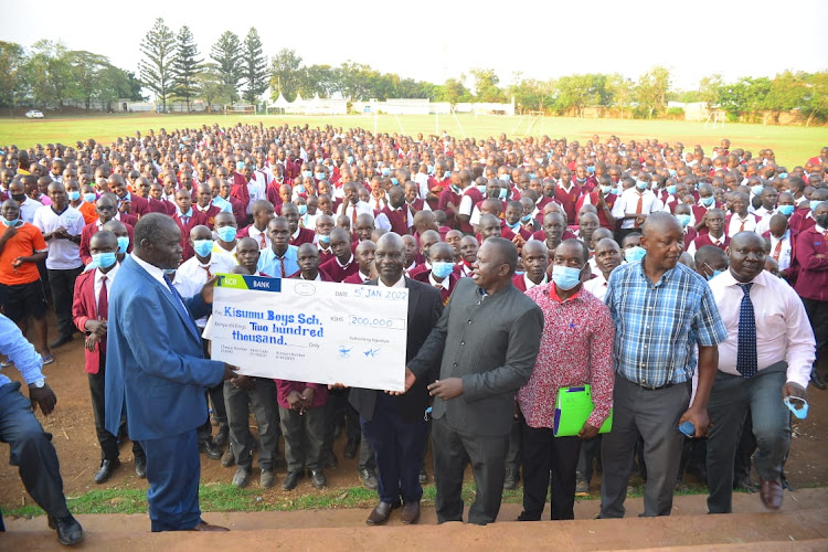 Kisumu Boys High School Alumni Association president James Aggrey Mwamu hands over Sh200,000 dummy cheque to the school principal Peter Obuogo.