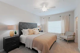 Model bedroom with light beige carpet, light gray walls, white trim and doors, and a white ceiling fan