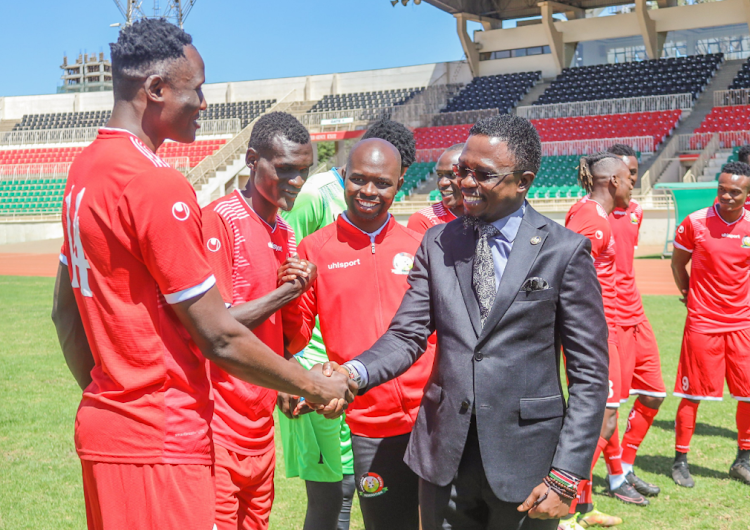 Sports CS Ababu Namwamba shakes hands with Harambee Stars skipper Michael Olunga during a visit to the team's training camp at Nyayo Stadium