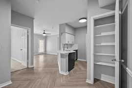 Spacious, modern apartment interior featuring an open-plan kitchen with black appliances and white cabinets, leading to a living area.