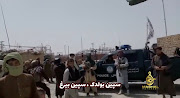 People stand in front of a vehicle as an Islamic Emirate of Afghanistan and a Pakistan's flag flutter in front of the friendship gate of Afghanistan and Pakistan at the Wesh-Chaman border crossing, Spin Boldak, Afghanistan July 14, 2021, in this screen grab obtained from a video. 