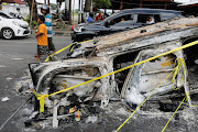 People pass by a damaged car following a riot and stampede following a soccer match between Arema vs Persebaya outside the Kanjuruhan stadium in Malang, East Java province, Indonesia, October 2, 2022.