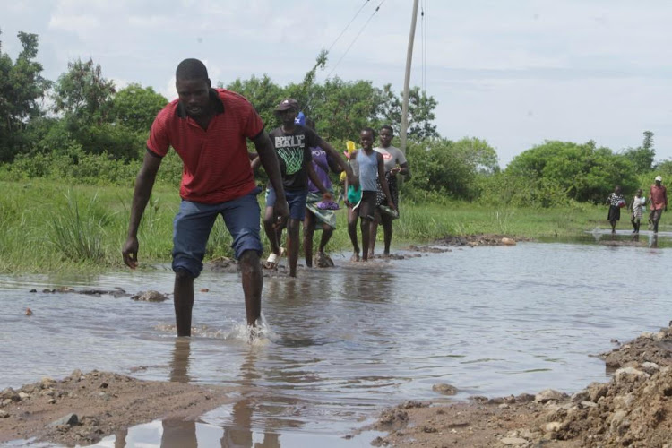 Residents of Kabuto walk across flooded road as heavy downpour has invaded the area