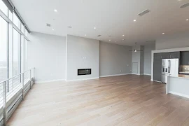 Large open concept living room with wood-inspired flooring, light walls, high ceilings, fireplace, and access to the kitchen