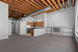 Modern apartment interior with open floor plan, exposed wooden beams, and a kitchen with stainless steel appliances.