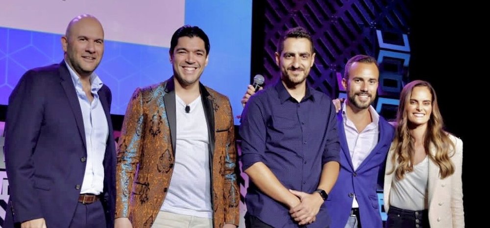 Un grupo de cuatro hombres y una mujer de pie sobre un escenario en una conferencia de tecnología.