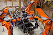 Robotic arms operate on the chassis frame of a new BMW i3 battery-powered automobile.