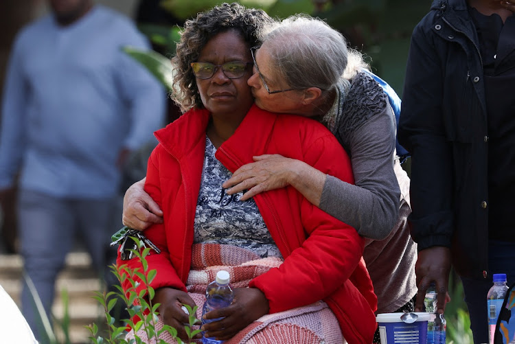 A woman comforts a family member of a construction worker near the site where rescuers are searching for people trapped under a building that collapsed in George.