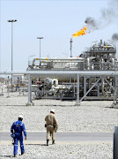 Two oil workers approach the installation during the opening ceremony of Majnoon oil field, east of Basra, Iraq. Opec producers have no plans to squeeze output as the oil price takes a nosedive to a price per barrel last seen a decade ago and new players enter the market