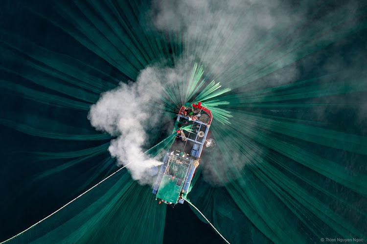 "The soft light of a new day illuminates the smoke from the fishing boat engine and the shape of green nets moving underneath the water surface when local fishermen pull in their nets. Many local fishing families along the coastline of Phu Yen province will follow the near-shore currents to catch anchovy during peak season. Salted anchovy is the most important raw ingredient used to create traditional fish sauce - the spirit of Vietnamese cuisine."