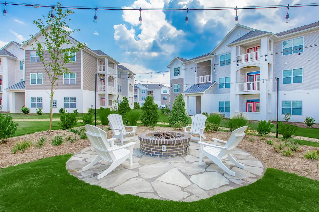 Firepit area with conversational white loungers and beige brick apartment building in the background