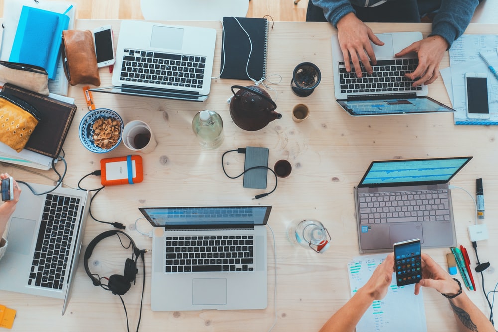 office table top with assorted laptops, headphones, external hard disks and other office ware